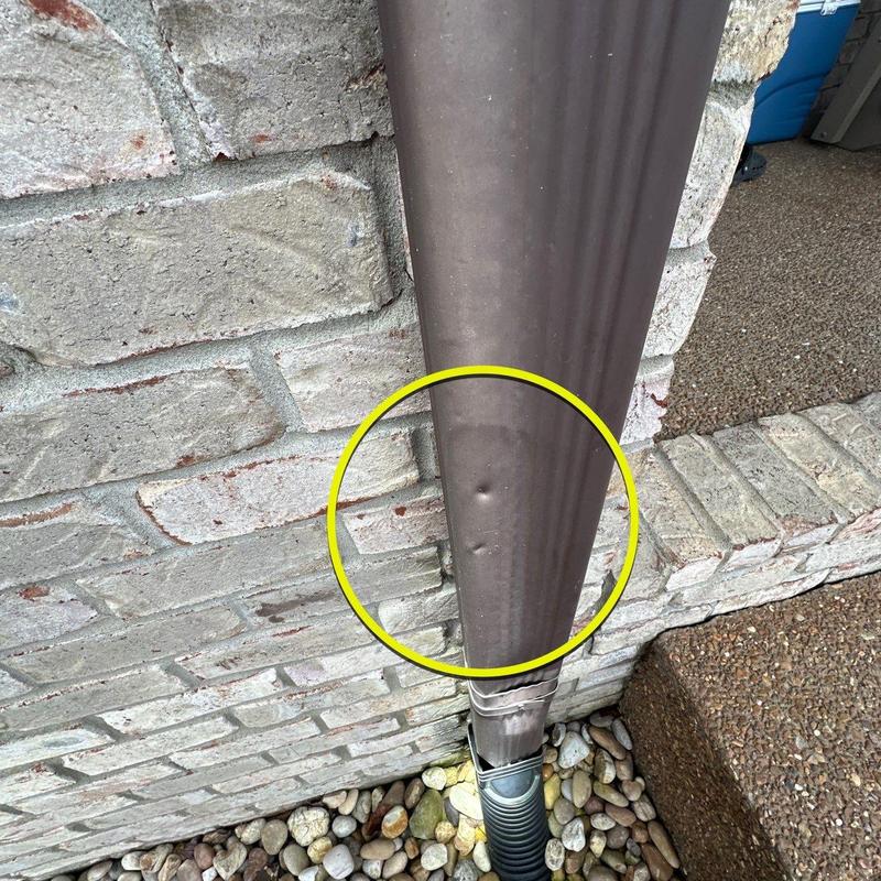 Downspout with dent damage near foundation wall