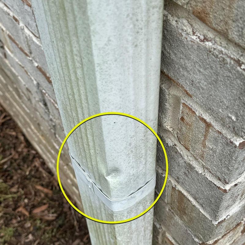Downspout dented and secured with metal strap near brick wall