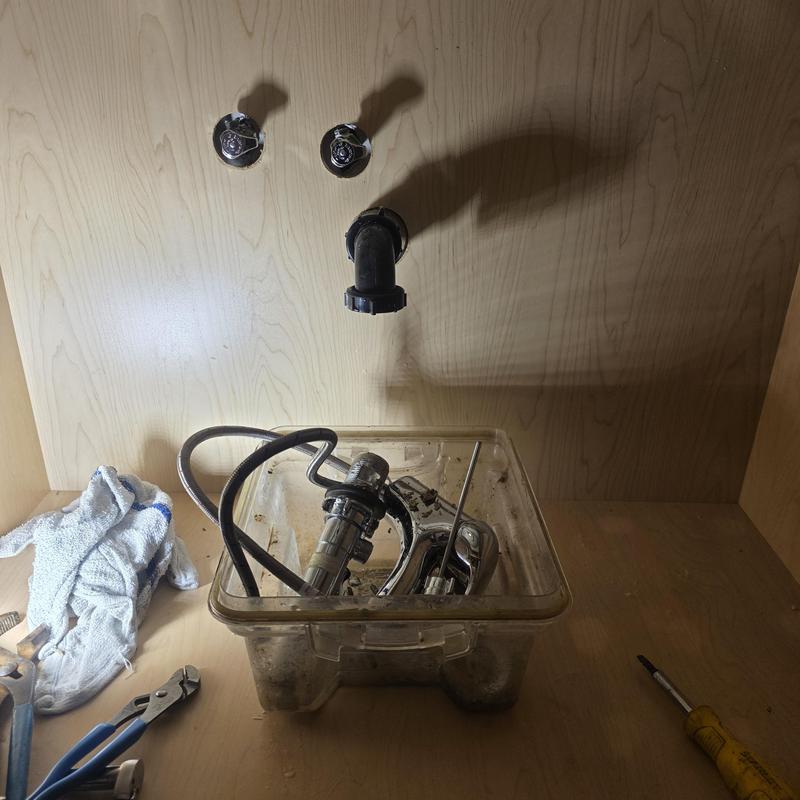 Bathroom sink faucet removed under cabinet with parts