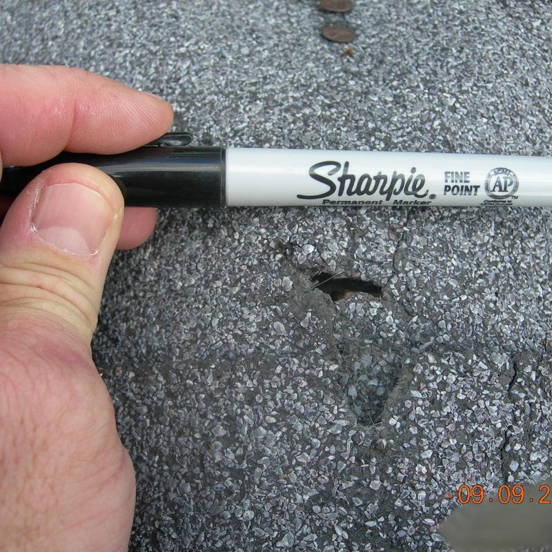 Asphalt shingle hail damage with hole and marker for scale Asphalt shingle hail damage with hole and marker for scale