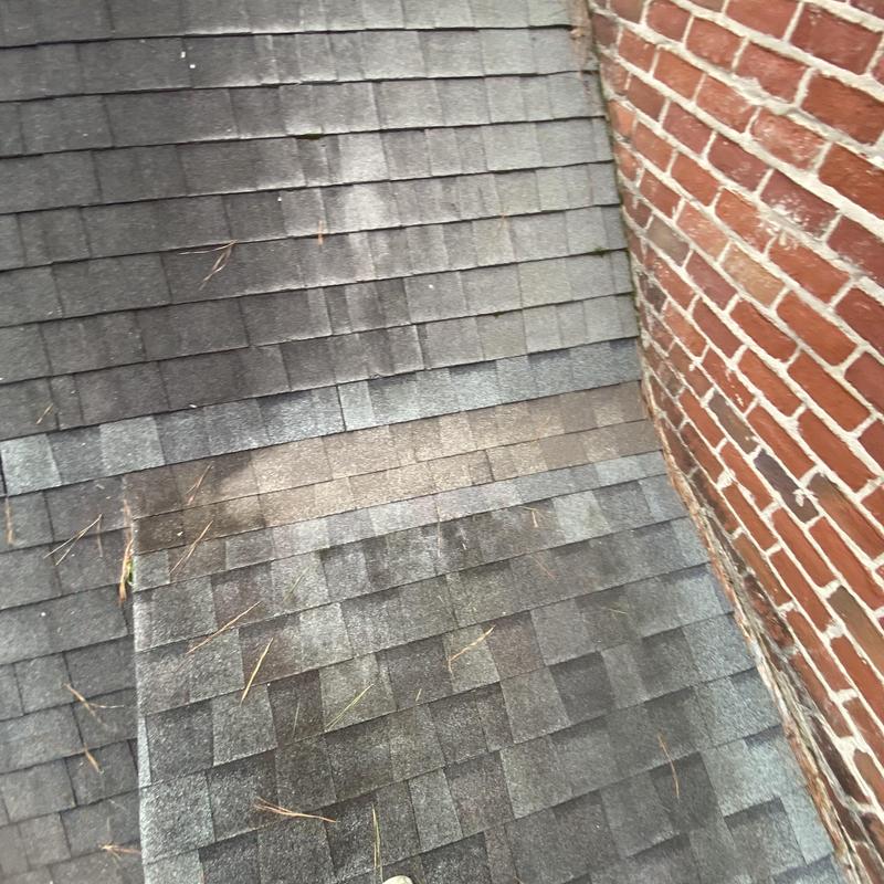 Asphalt shingle roof near brick chimney with wear signs