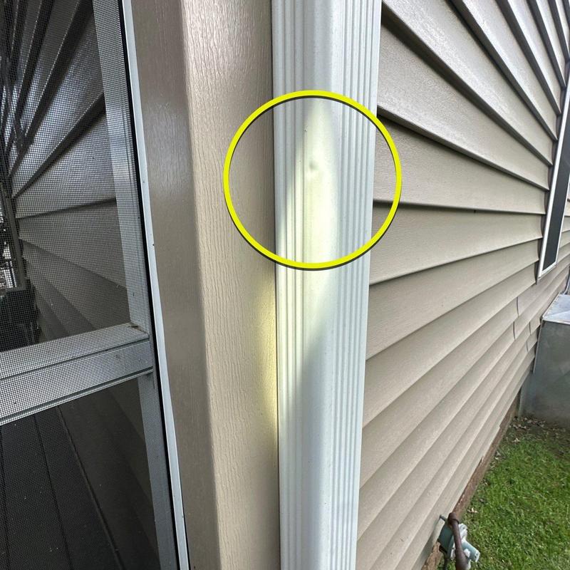 Vinyl downspout dent with circled damage on house exterior