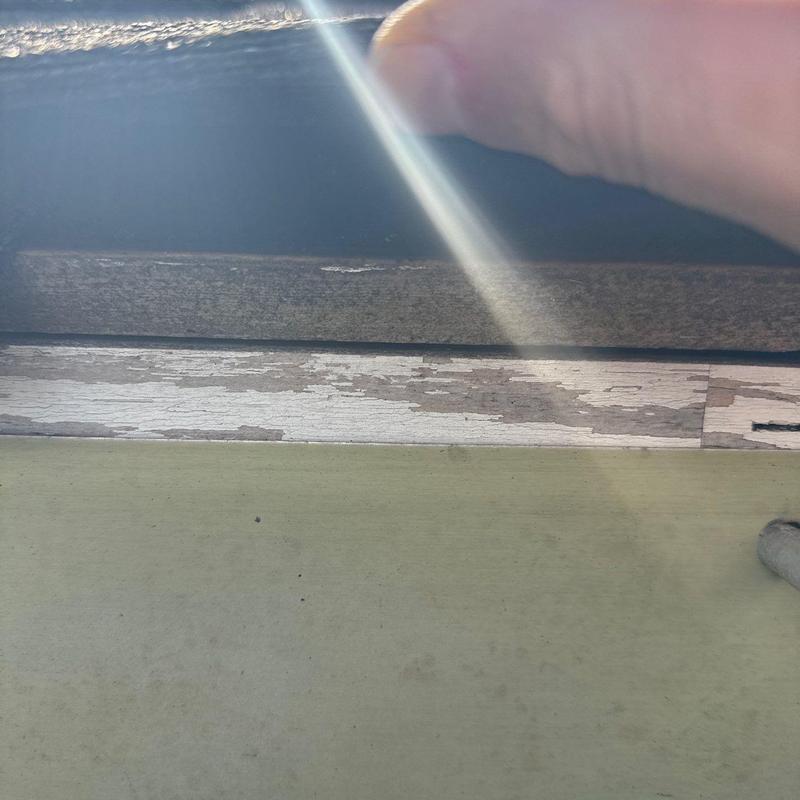 Window frame paint peeling with hand examining sunlight