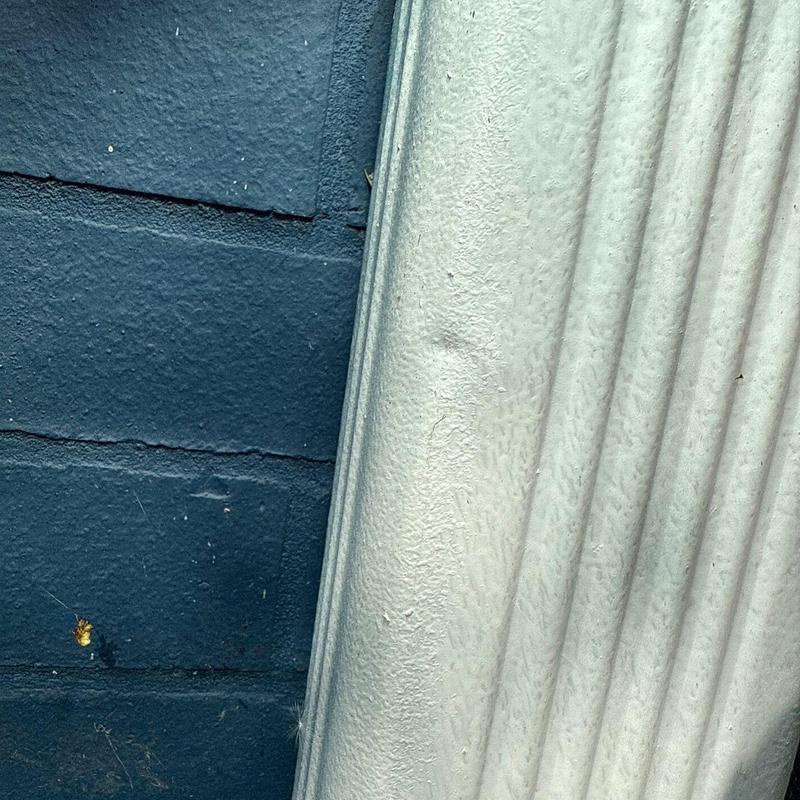 Downspout with dents against blue brick wall