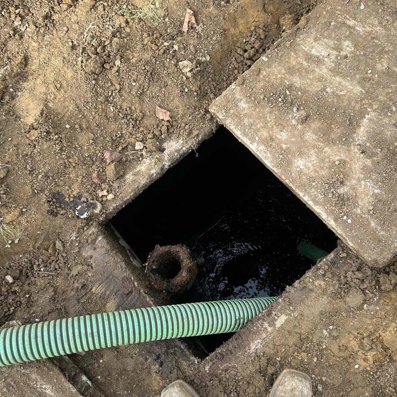 Septic tank with green pump hose in dirt excavation