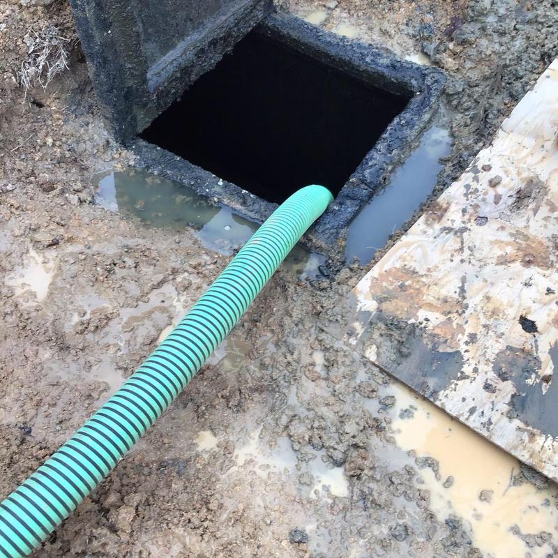 Septic tank with green suction hose in muddy ground