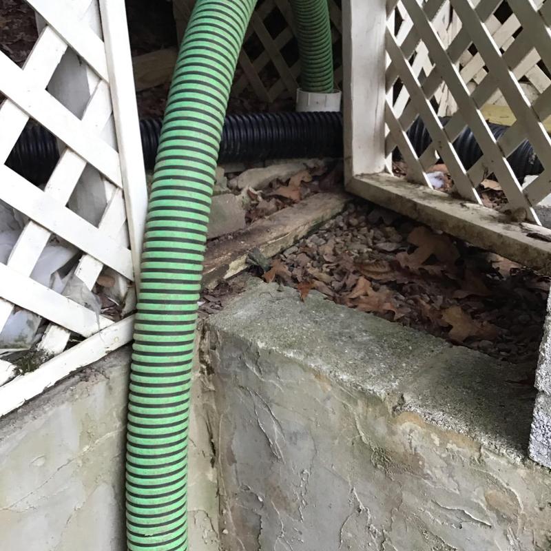 Septic tank pumping with green suction hose in crawl space