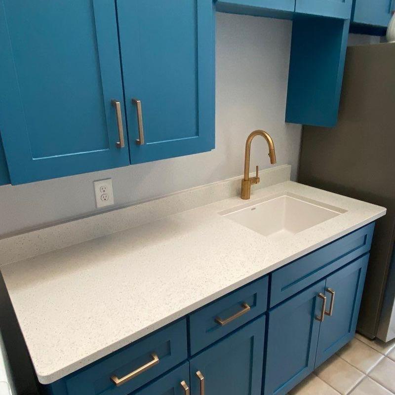 Laundry room quartz countertop with brass faucet and blue cabinets