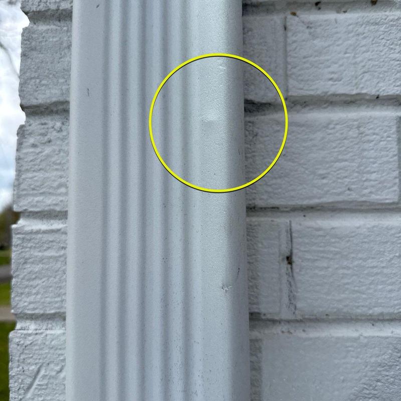 Downspout dent with circled damage on white brick wall