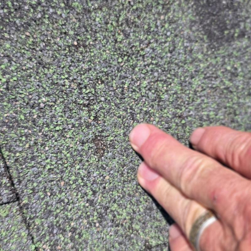 Roof shingles hail impact damage close-up with hand