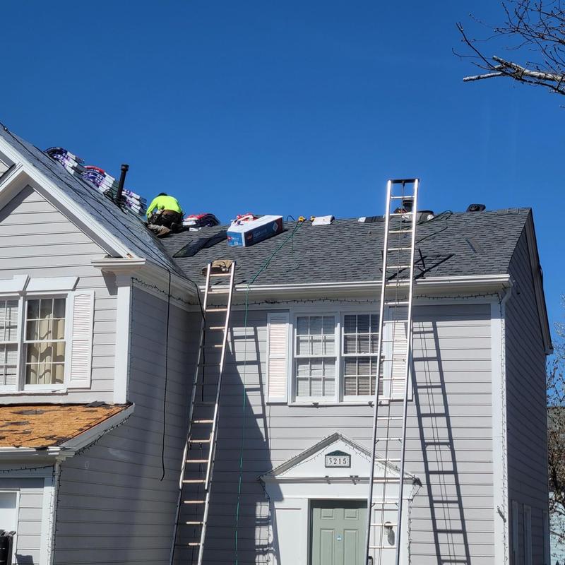 Asphalt shingle roof installation with ladders and worker