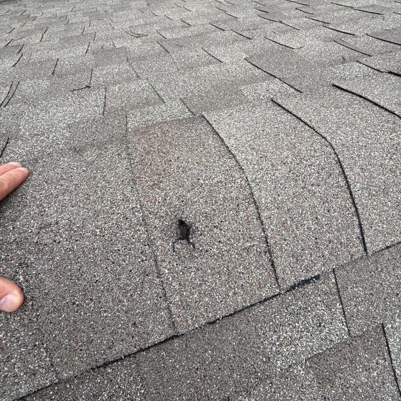 Asphalt shingle roof with hail damage hole close-up