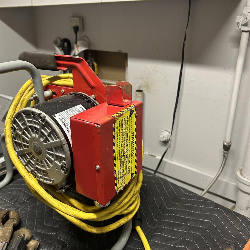 Drain cleaning machine with yellow power cord in bathroom