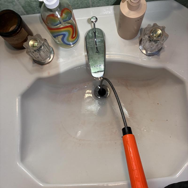 Basin drain cleaning with plumbing snake in bathroom sink