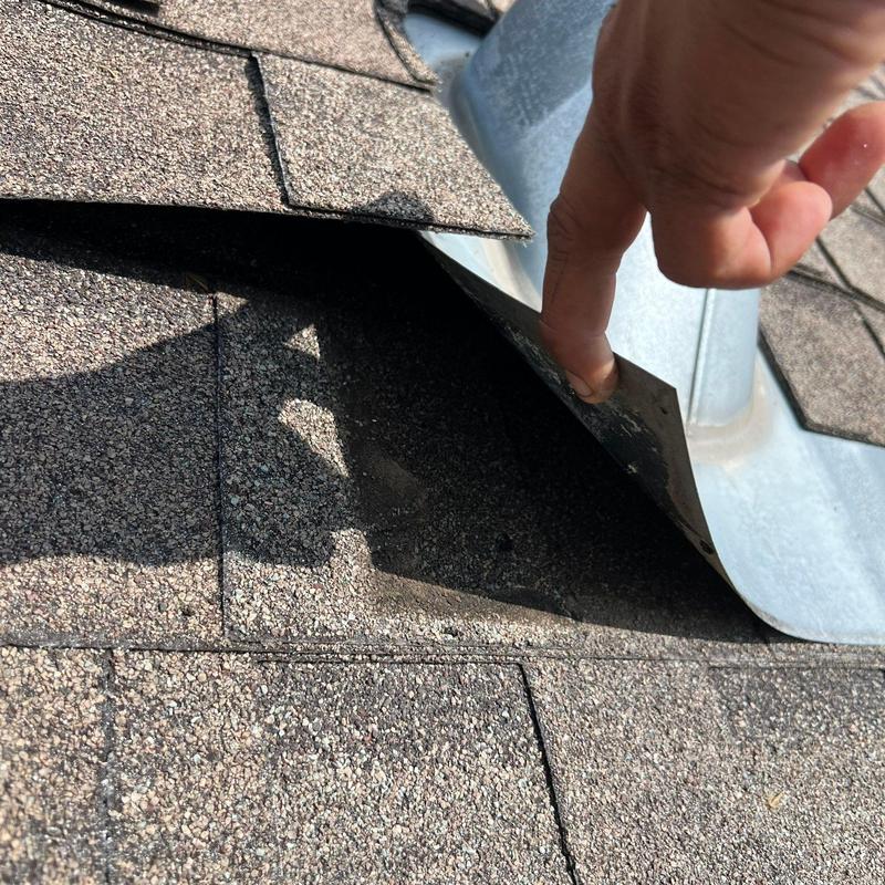 Roof flashing inspection showing lifted shingle edge