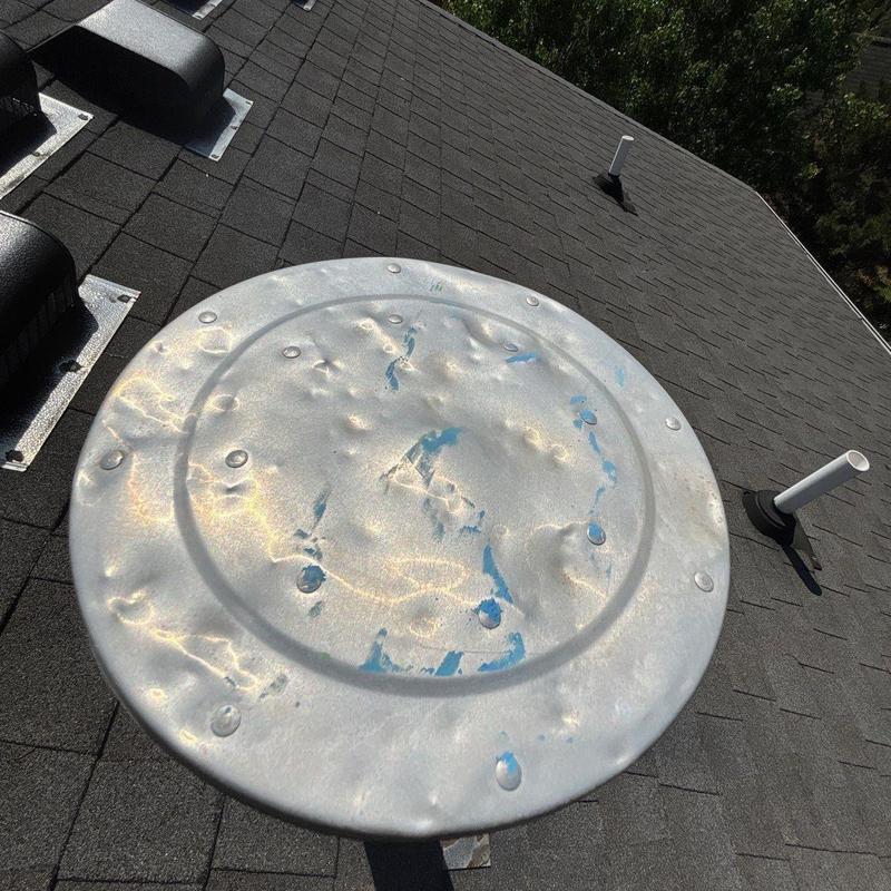 Metal vent cover with hail damage on asphalt roof