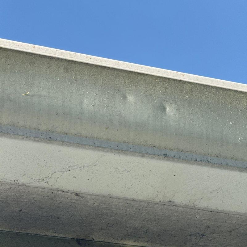 Metal gutter with visible dents under blue sky