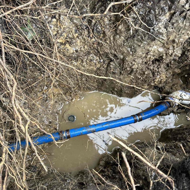 Blue underground pipe in muddy trench with water Blue underground pipe in muddy trench with water