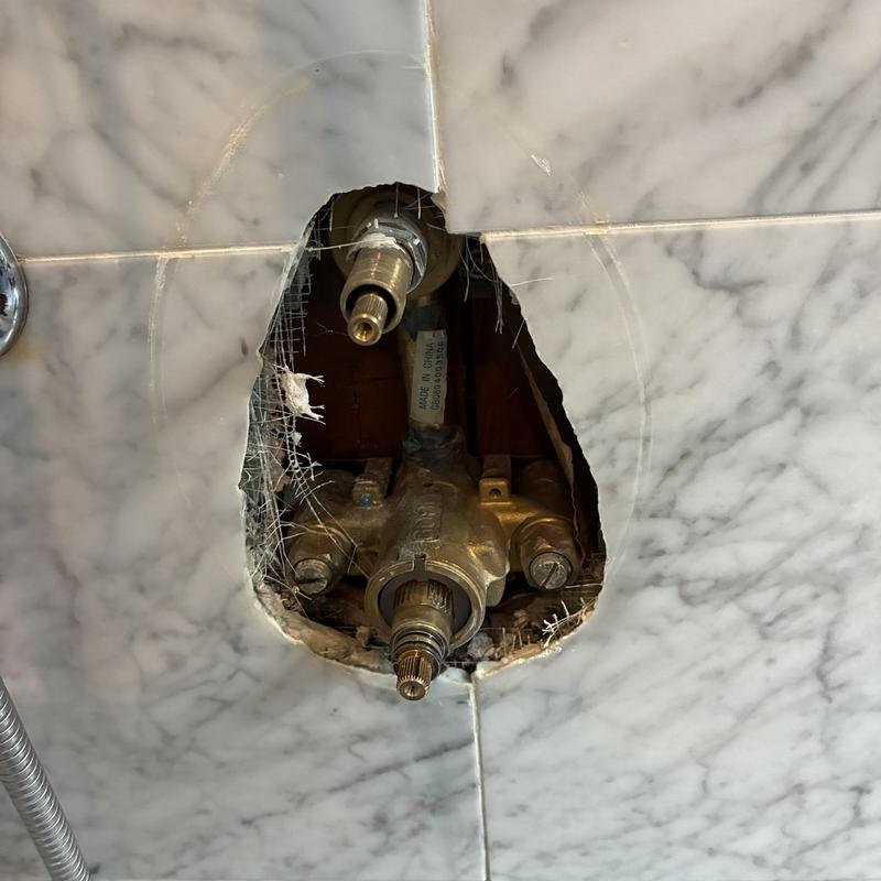 Shower valve assembly exposed behind marble tile wall