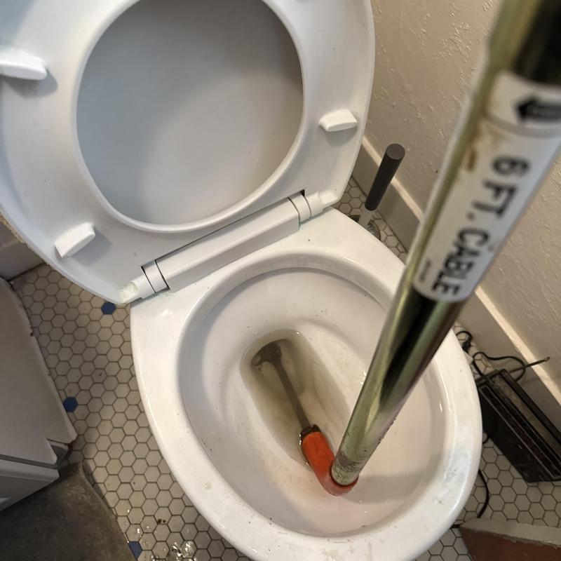 Toilet drain auger clearing blockage in residential bathroom