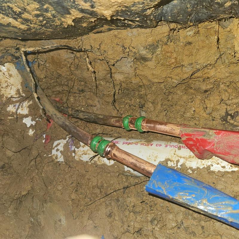 Copper water lines with green compression fittings in soil