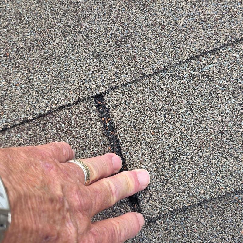 Asphalt shingles close-up with hand inspecting hail damage