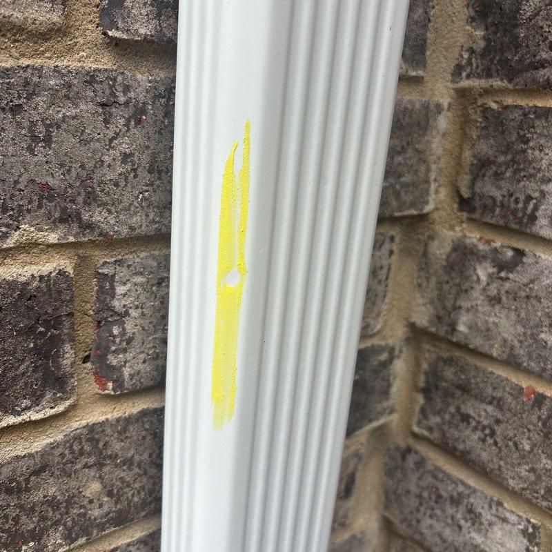 Downspout with dent and yellow paint mark on brick wall