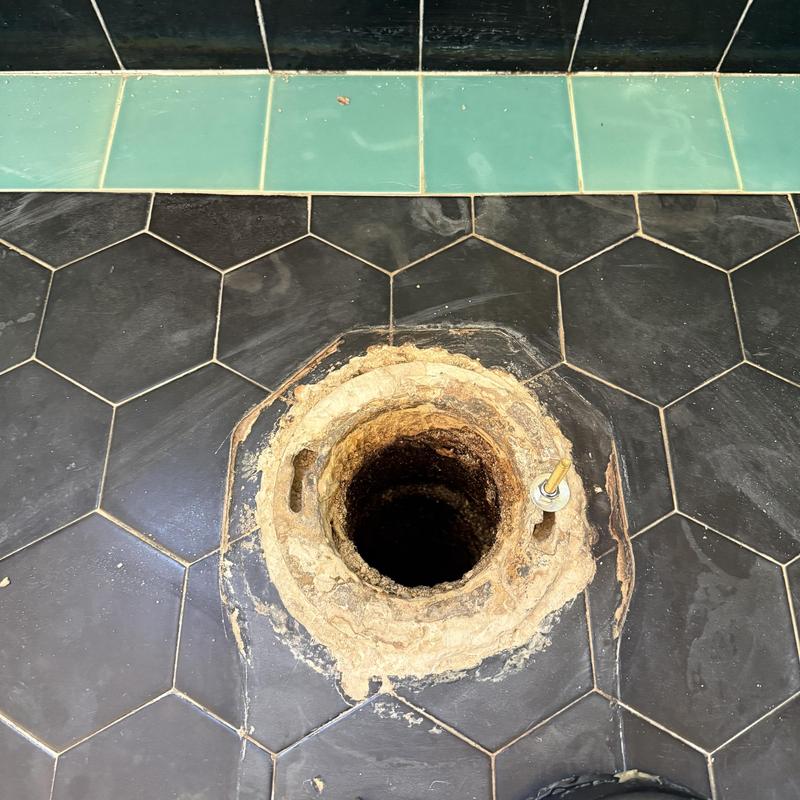 Toilet flange on black hex tile floor