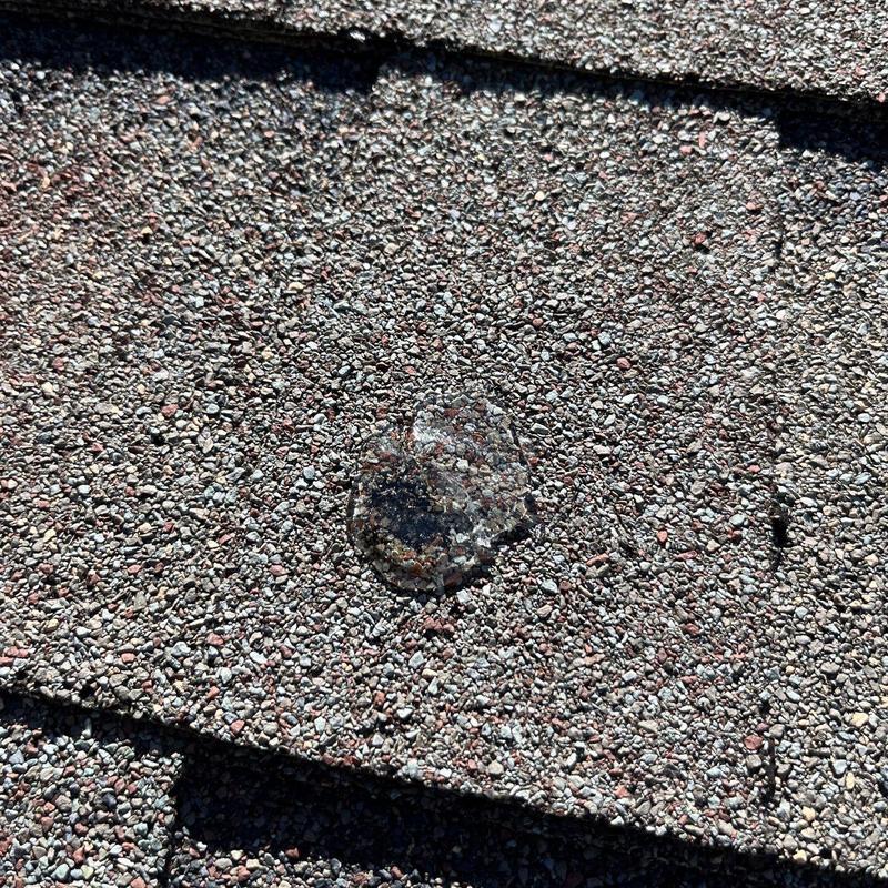 Asphalt roof shingle with hail damage impact spot