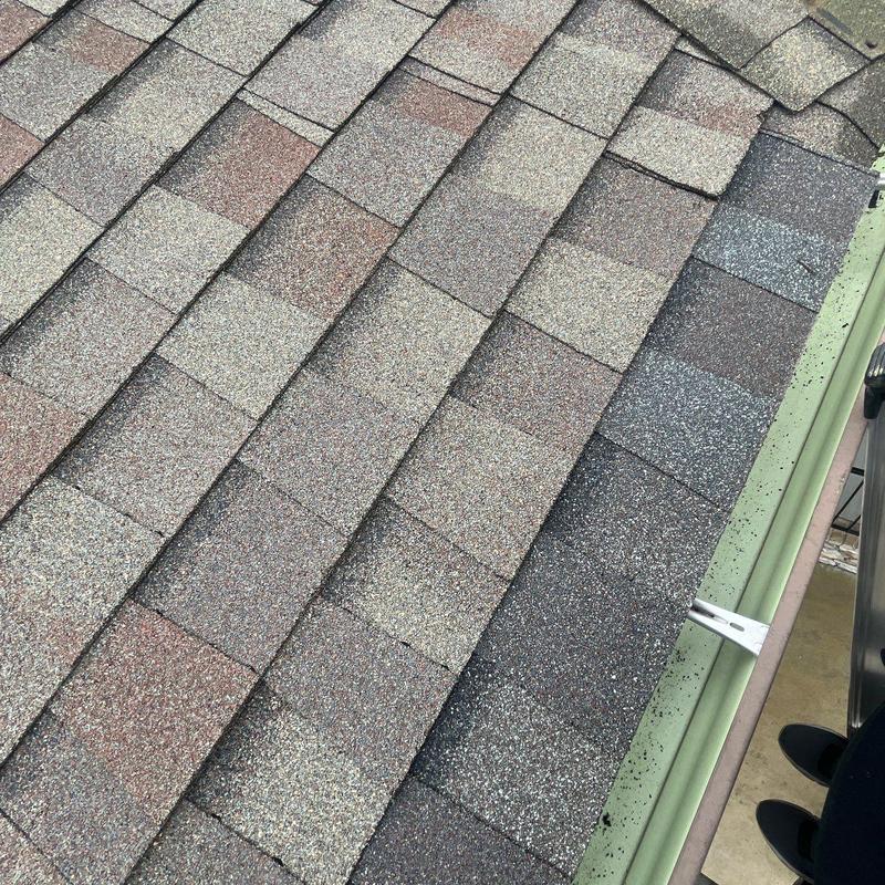 Asphalt roof shingles with hail impact damage near gutter