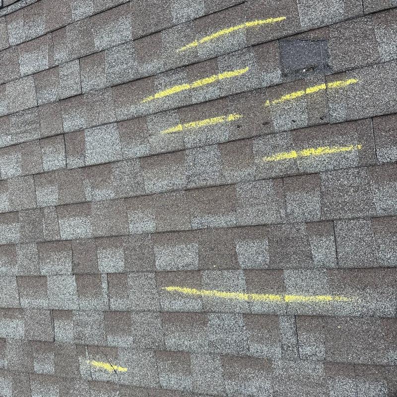 Asphalt shingles with hail damage marked by yellow paint