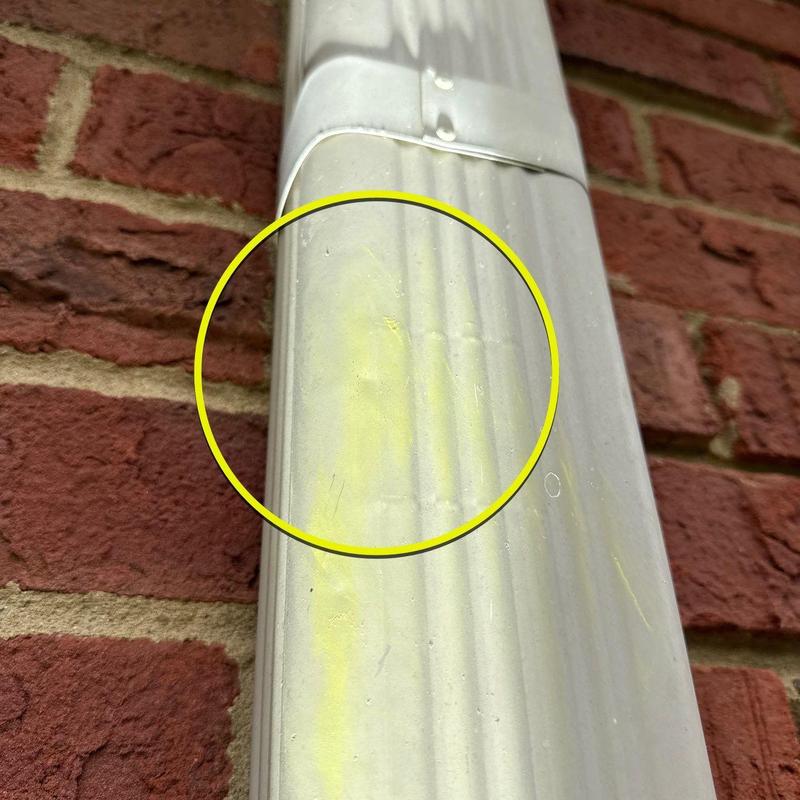 Downspout with dented area marked by yellow circle