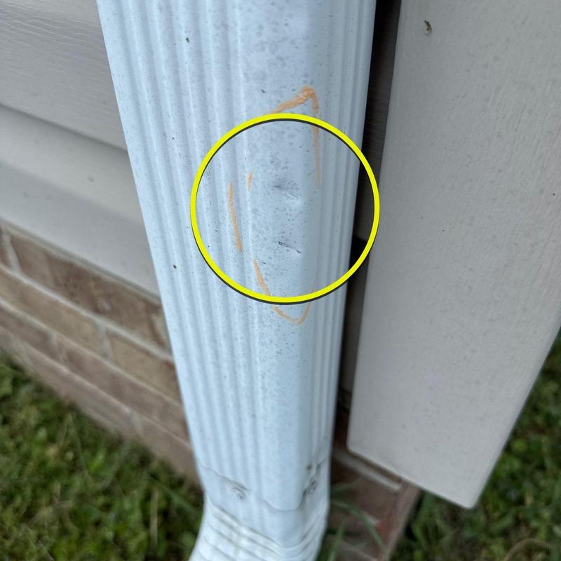 Downspout dent with orange marking on white siding background