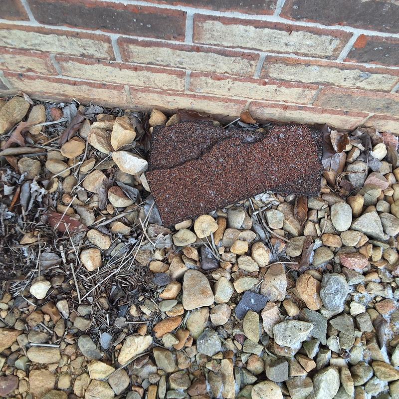 Asphalt roof shingle detached near brick foundation and stones