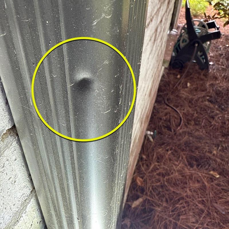 Metal downspout with dent inside yellow circle