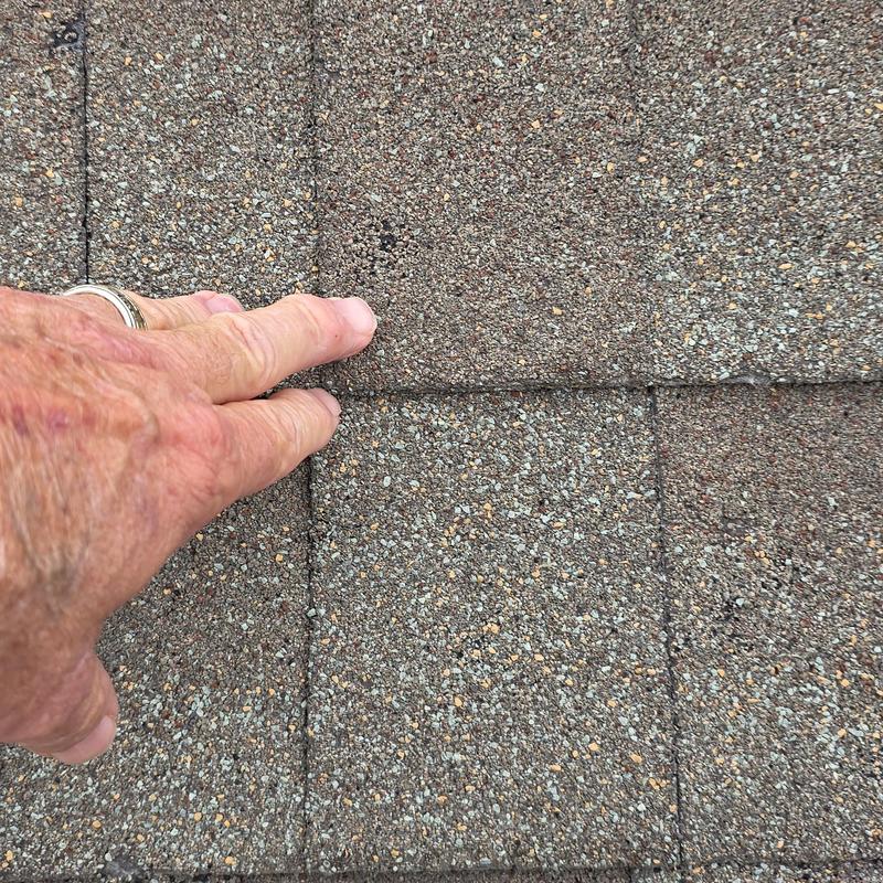 Asphalt shingle roofing hail damage close-up with hand