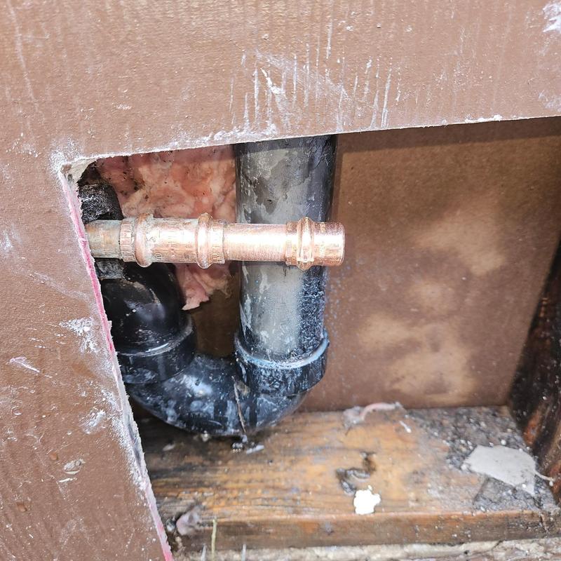 Copper hot water line near black drain pipe inside wall