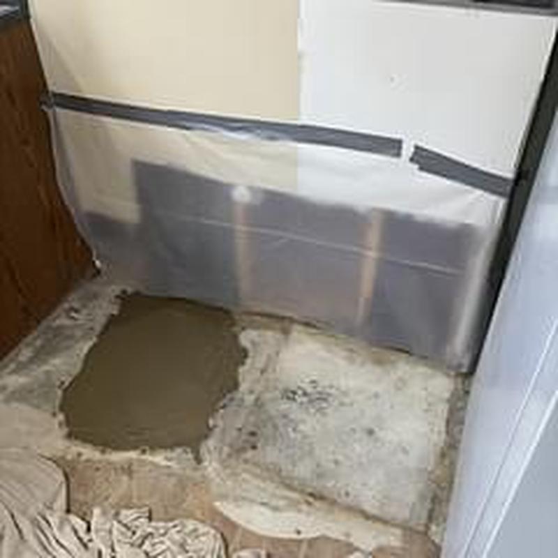 Concrete slab with fresh patch and exposed pipes behind plastic