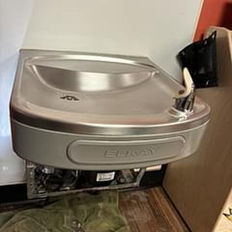 Drinking fountain with exposed plumbing below wall-mounted unit