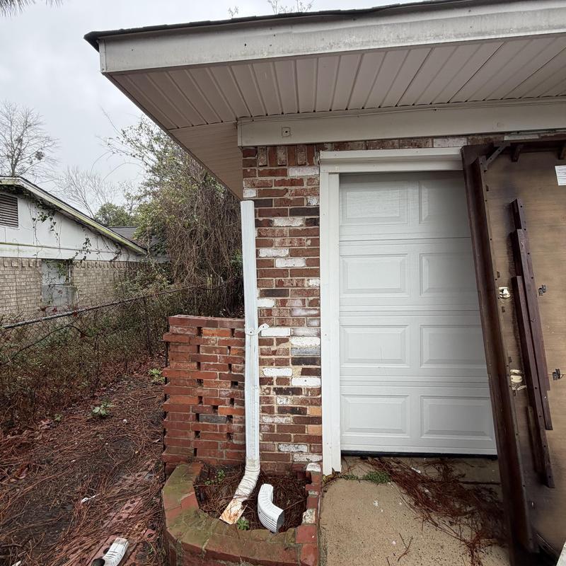 Damaged white downspout and brick planter wall near garage door
