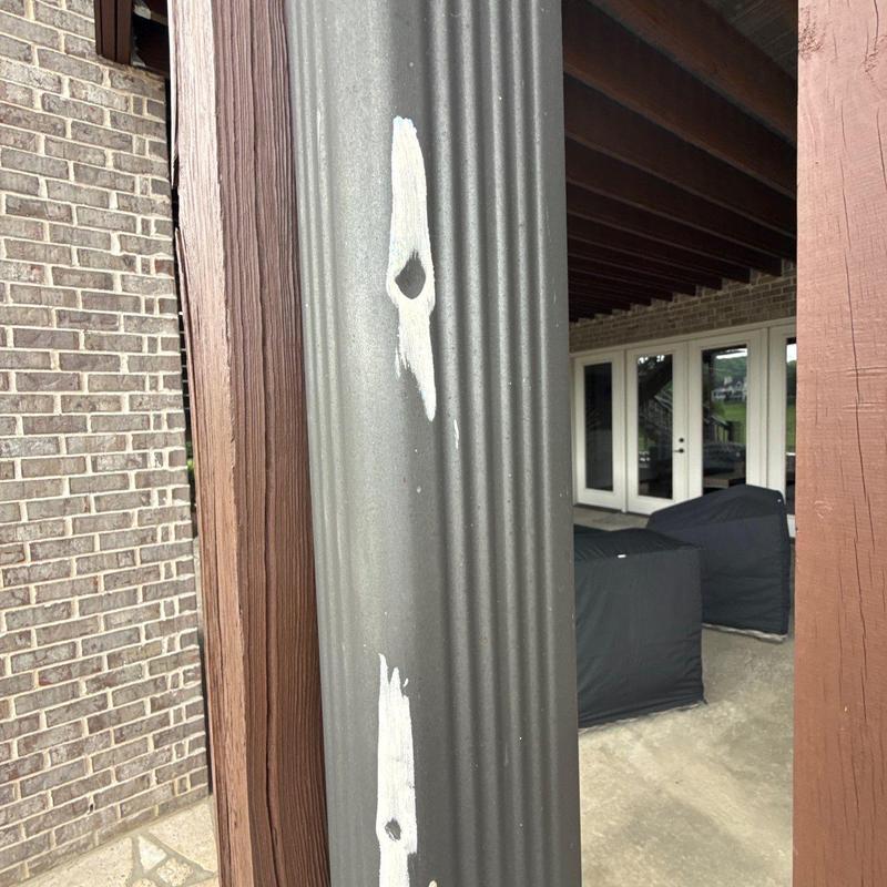 Metal downspout with corrosion and paint damage outdoors