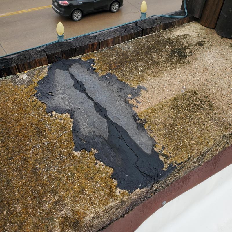 Flat roof patch with cracked sealant and moss buildup