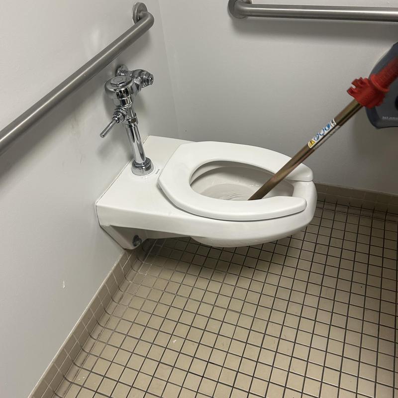 Wall-mounted toilet with drain snake in commercial restroom