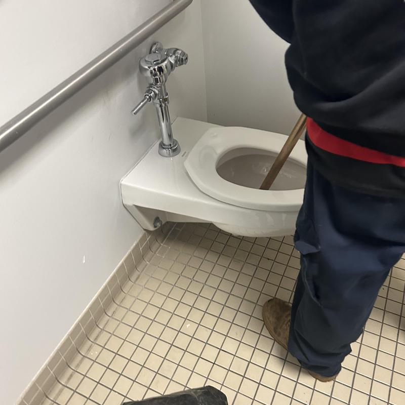 Wall-mounted toilet being drained with auger in bathroom