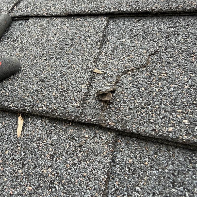Roof shingle with popped nail and cracked granules