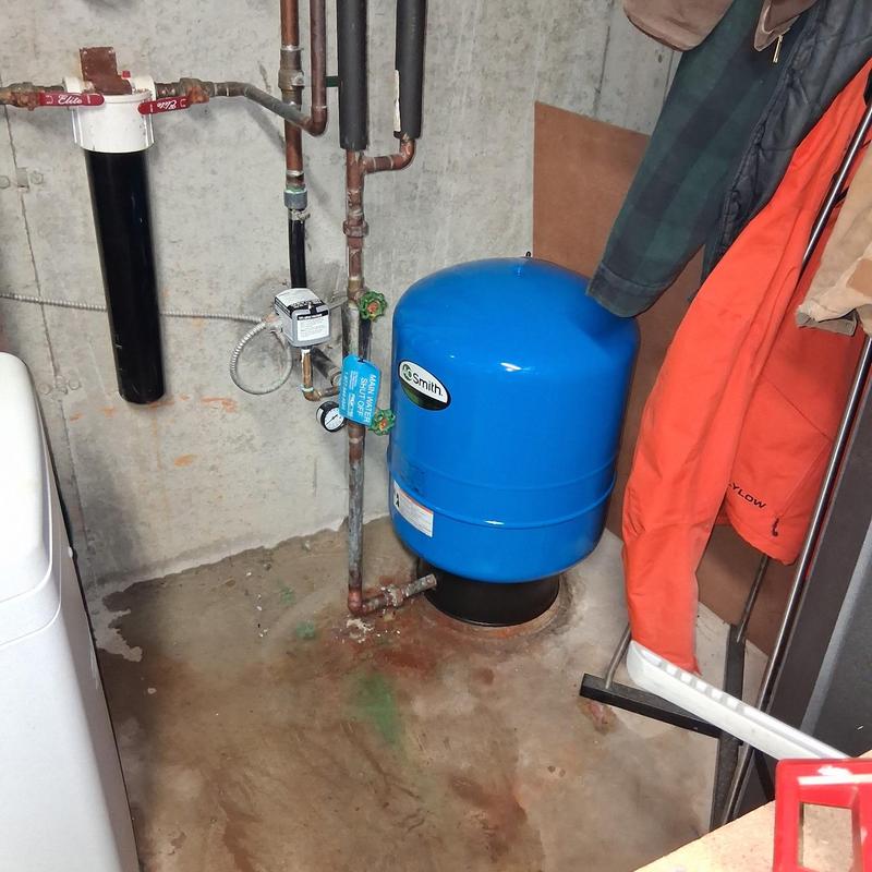 Bladder tank with connected plumbing in basement corner