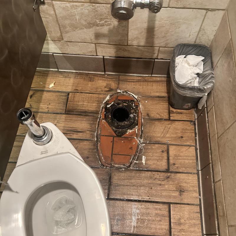 Toilet flange and base pipe exposed in restroom floor