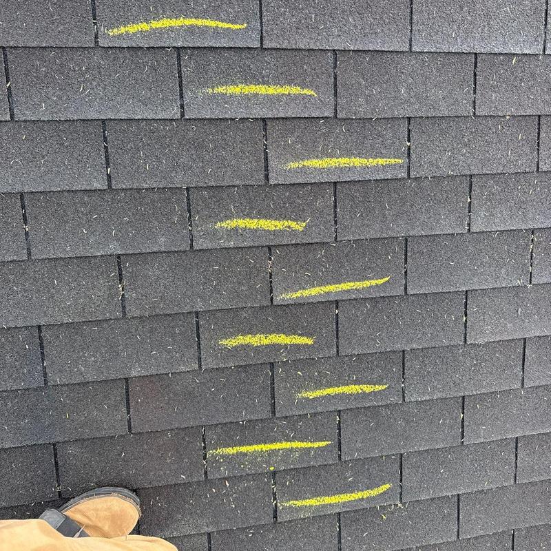 Asphalt shingles with yellow markings indicating damage