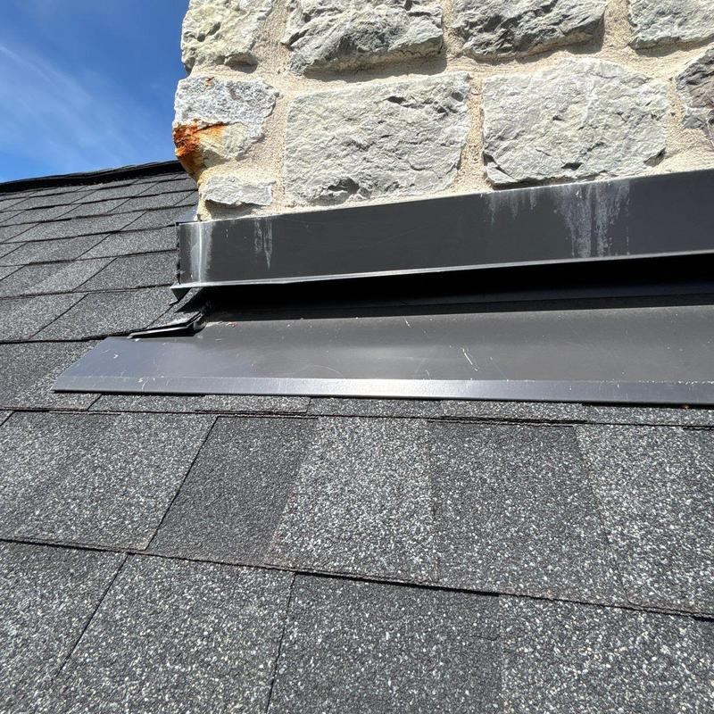 Step flashing on shingle roof near stone chimney