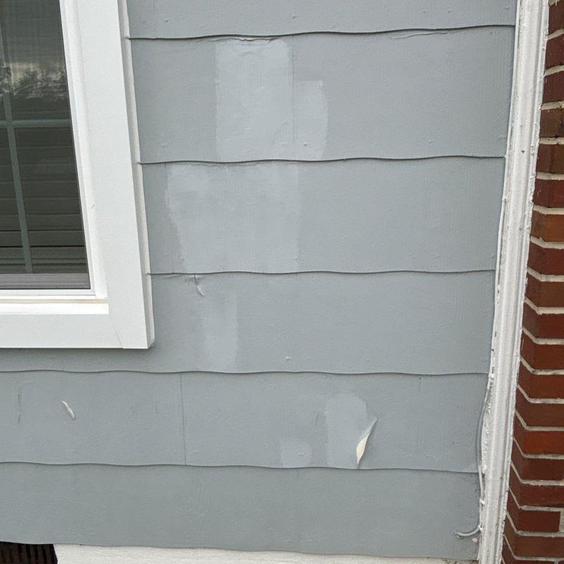 Exterior siding with peeling paint near window and brick wall